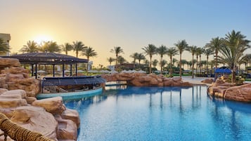 A swimming pool with rock formations, palm trees, and a gazebo.