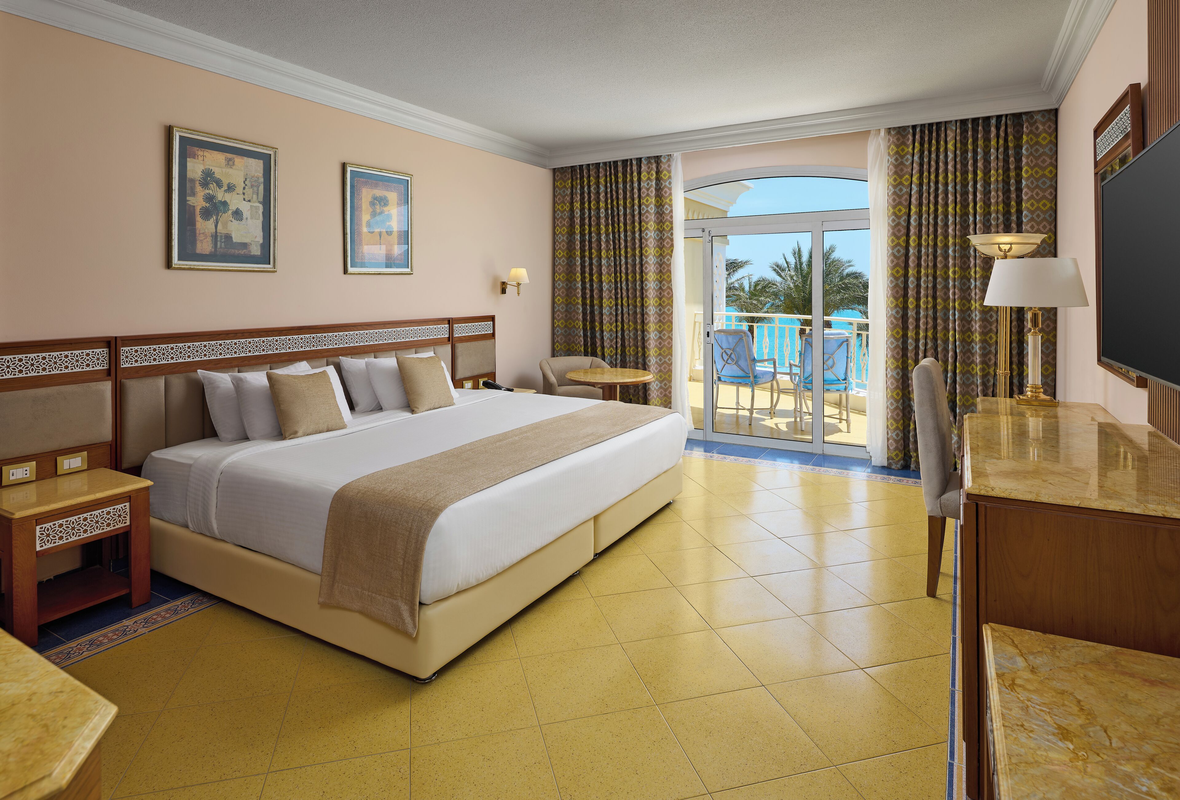 A hotel room with a large bed, a desk, a chair, a TV, and a balcony with a pool view.