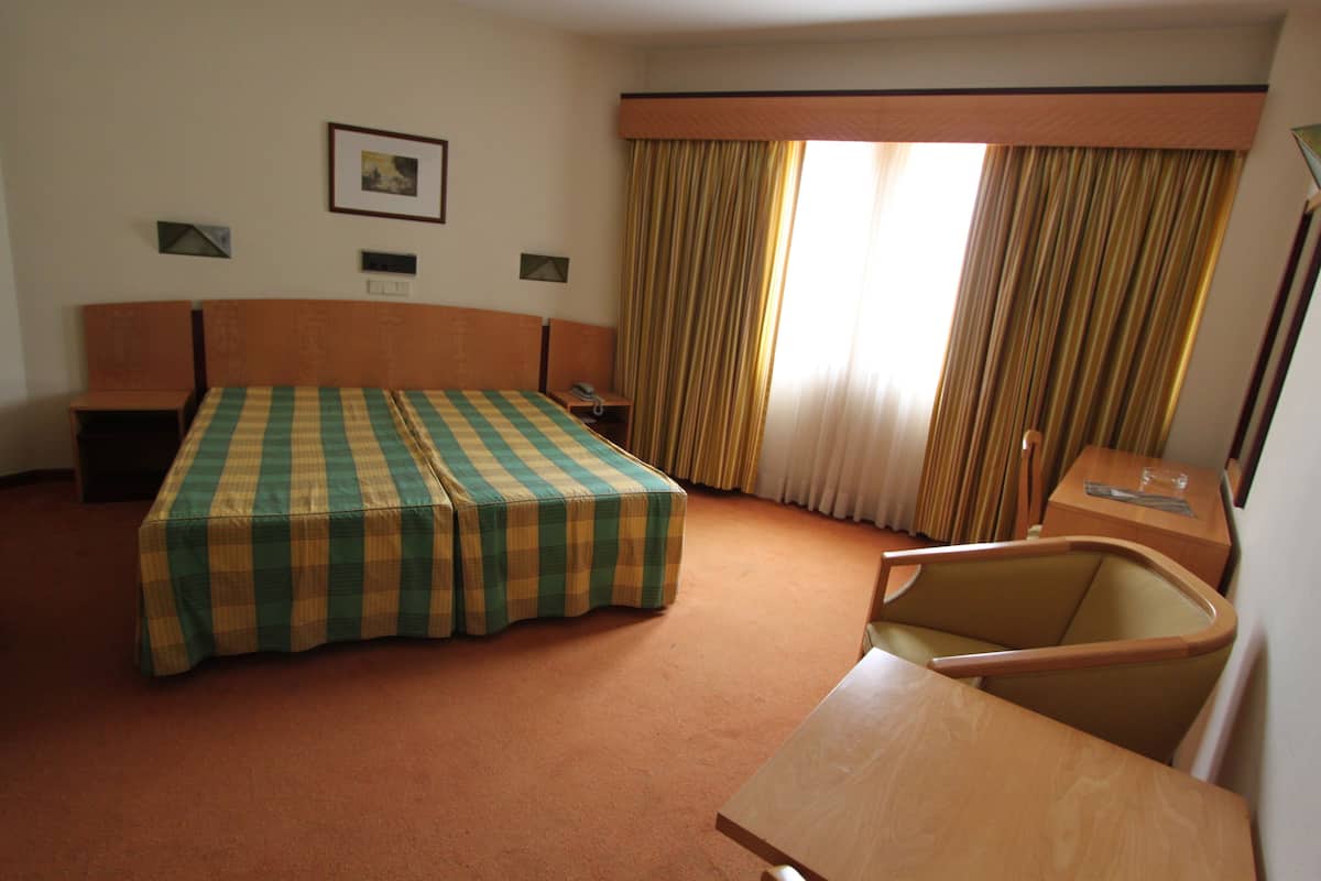Een hotelkamer met een groot bed, een houten bureau, een stoel en een raam met gordijnen.