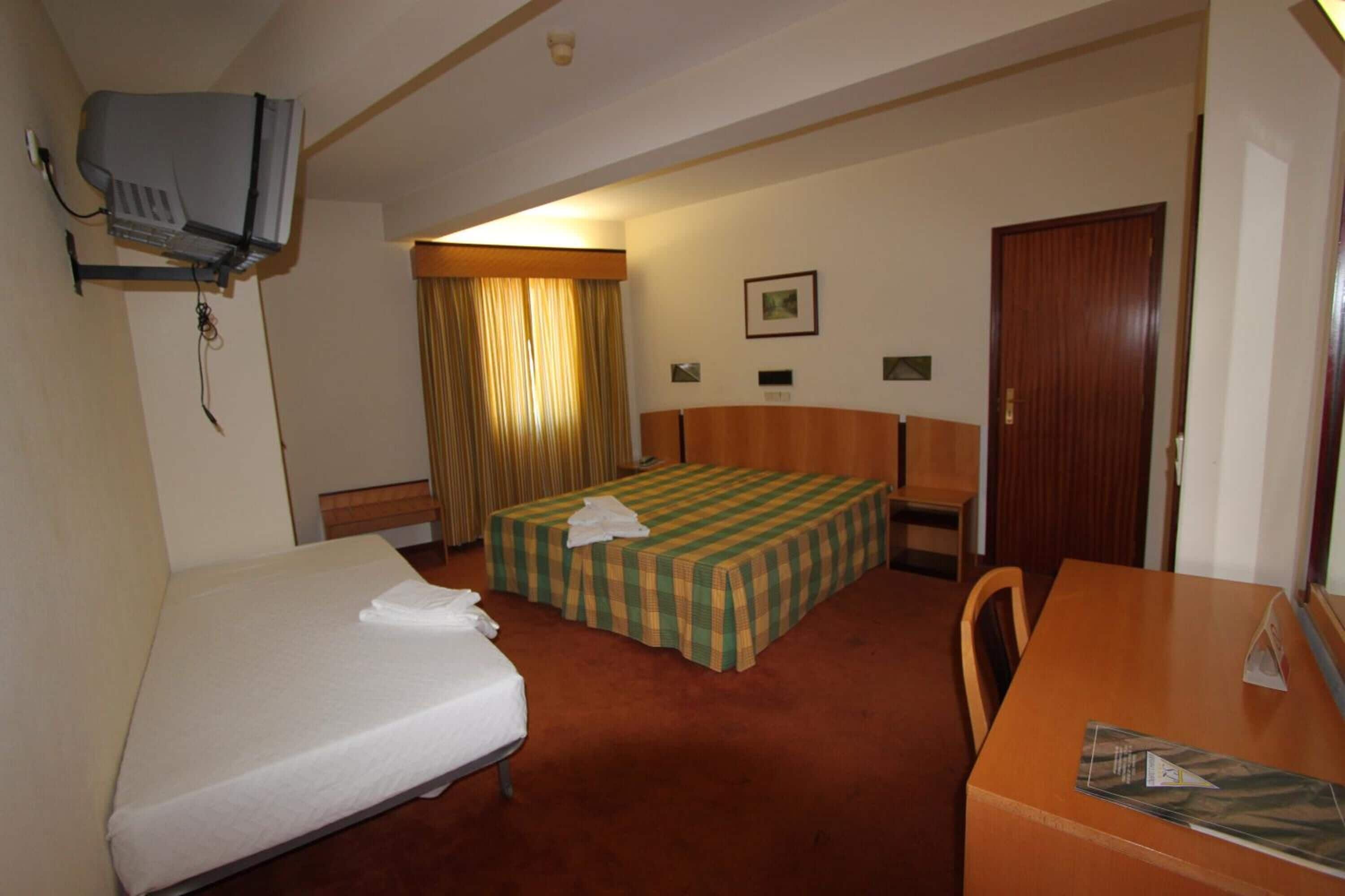 Een hotelkamer met een eenpersoonsbed, een bureau, een stoel, een aan de muur bevestigde televisie en een deur.