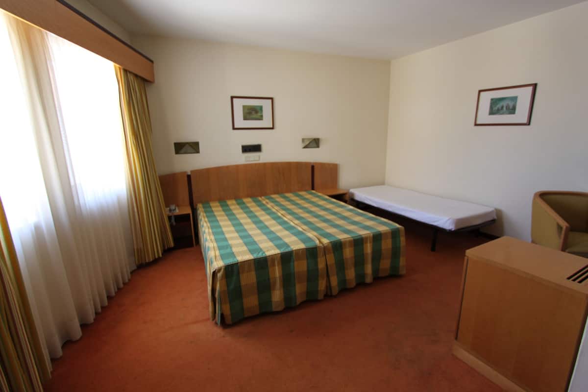 Hotelkamer met een enkel bed, een klein bureau, een stoel, een bank en twee ingelijste foto’s aan de muur.