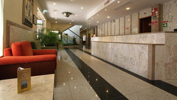 Een hotel lobby met een receptiebalie, een rode bank en een marmeren vloer.