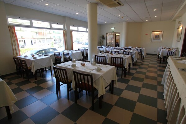 A dining area with multiple tables and chairs, a checkered floor, and large windows allowing natural light. - Hotel Sao Lourenco (Benavente)