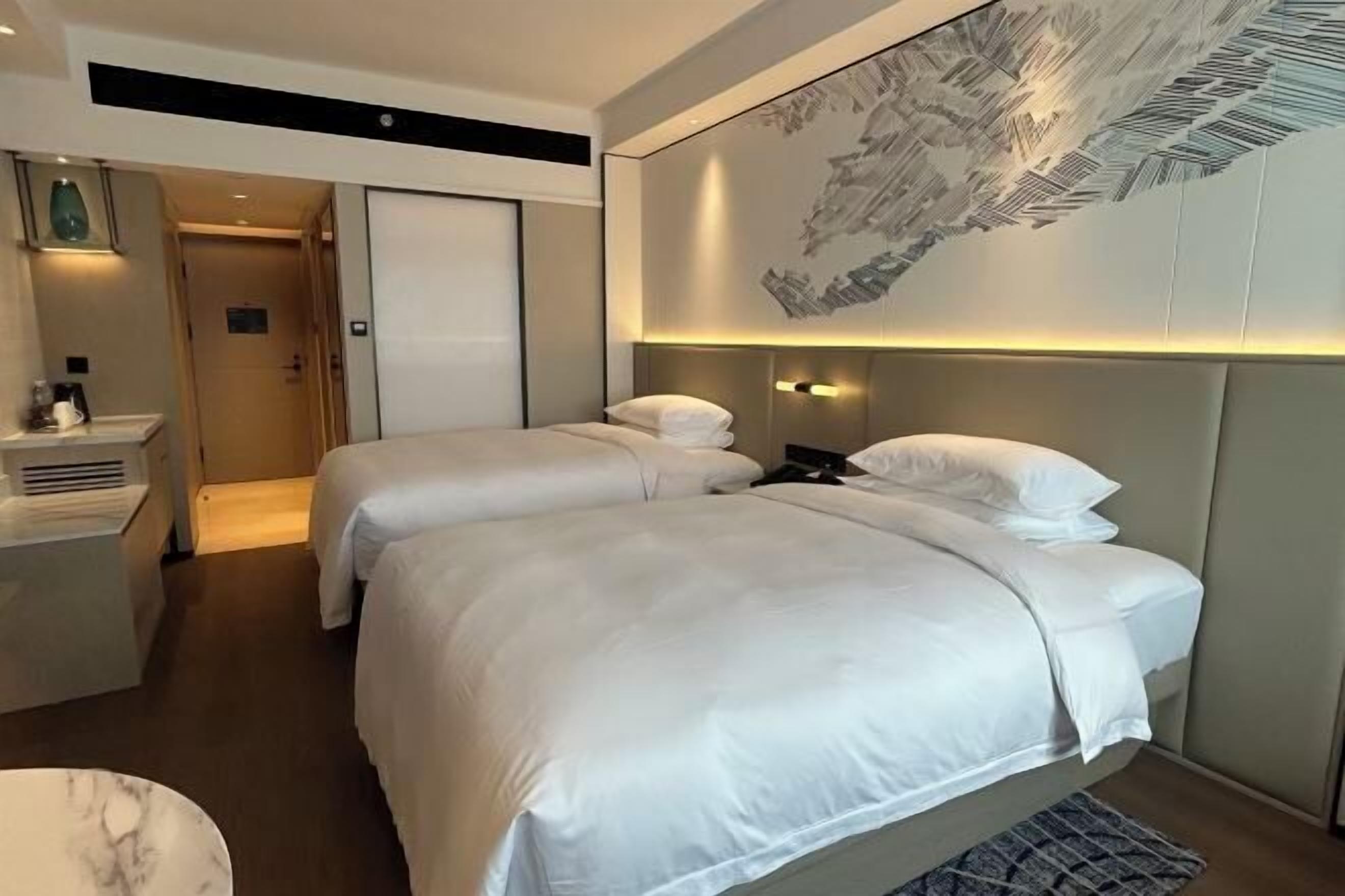 A hotel room with two beds, a desk, and a large artwork on the wall.