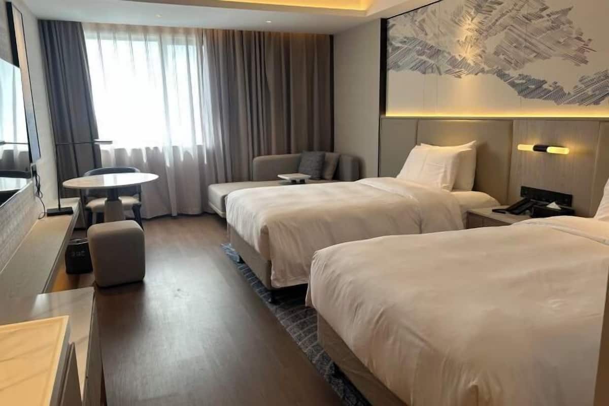A hotel room with two beds, a desk, a chair, a small table, and a large window with curtains.