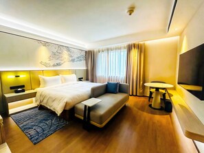 A modern hotel room with a large bed, a sofa, a small table, a TV, and a window with curtains.