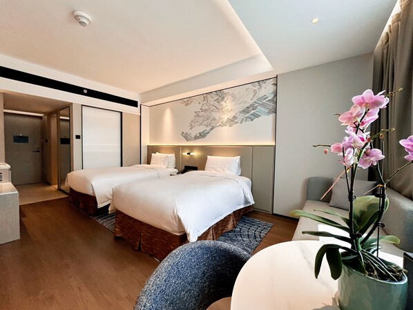 A hotel room with two beds, a large wall art piece, a potted orchid, and a view of the hallway.