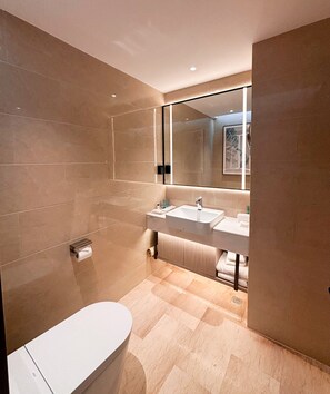 A modern bathroom with a large mirror, two sinks, a toilet, and a bathtub.