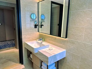 A modern bathroom with a large mirror, two round wall clocks, a white sink, and a towel rack.