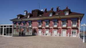 A multi-story building with a red facade, large windows, and a balcony. - Villa de Gijon (Gijon)