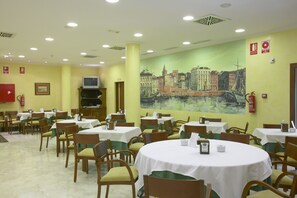 Un'area ristorazione con tavoli rotondi, sedie e un affresco raffigurante una veduta cittadina.