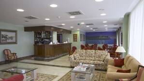 A hotel lobby with a reception desk, seating area, and a mural of a cityscape. - Villa de Gijon (Gijon)