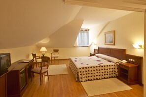 Una camera d'albergo con un letto, una scrivania, una sedia, un televisore e una finestra con tende.