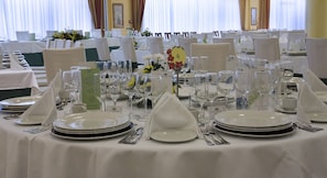 Une table de banquet dressée pour un événement formel, avec de nombreux couverts comprenant assiettes, couverts et verres à vin.