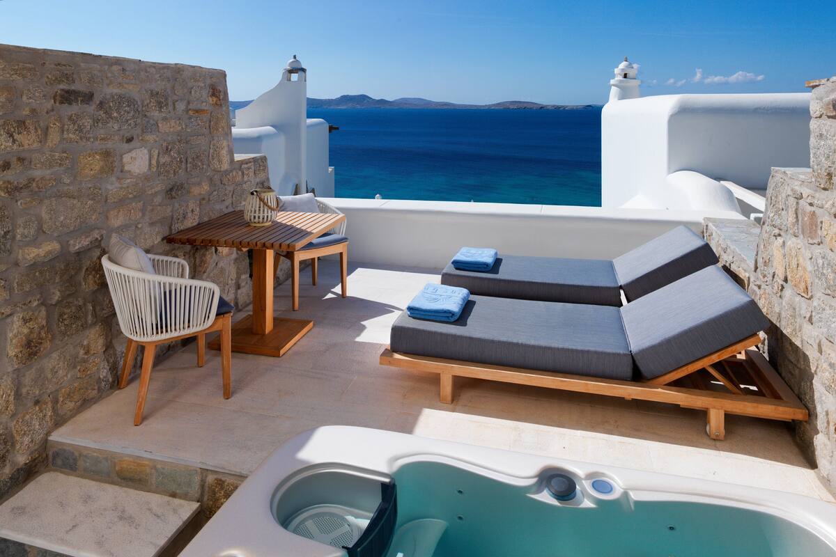 Een dakterras met een jacuzzi, lounge fauteuils, een tafel met stoelen en uitzicht op zee.