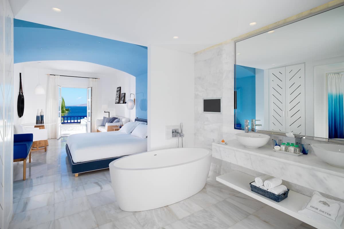Een moderne hotelkamer met een groot bed, een vrijstaand bad, een grote spiegel en uitzicht op de oceaan.