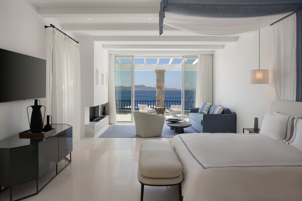 A modern hotel room with a large bed, a TV, a desk, and a balcony with a view of the sea. - Mykonos Grand Hotel & Resort (Mykonos)
