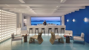 Un espace bar moderne avec un barman, des tabourets de bar blancs et une vue sur la mer.