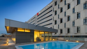 A modern hotel with a swimming pool, large windows, and a prominent building sign.