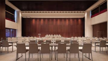 Une salle de conférence dotée de plusieurs tables et de chaises, d’une scène avec un décor en bois et d’un plafond haut avec des luminaires encastrés.