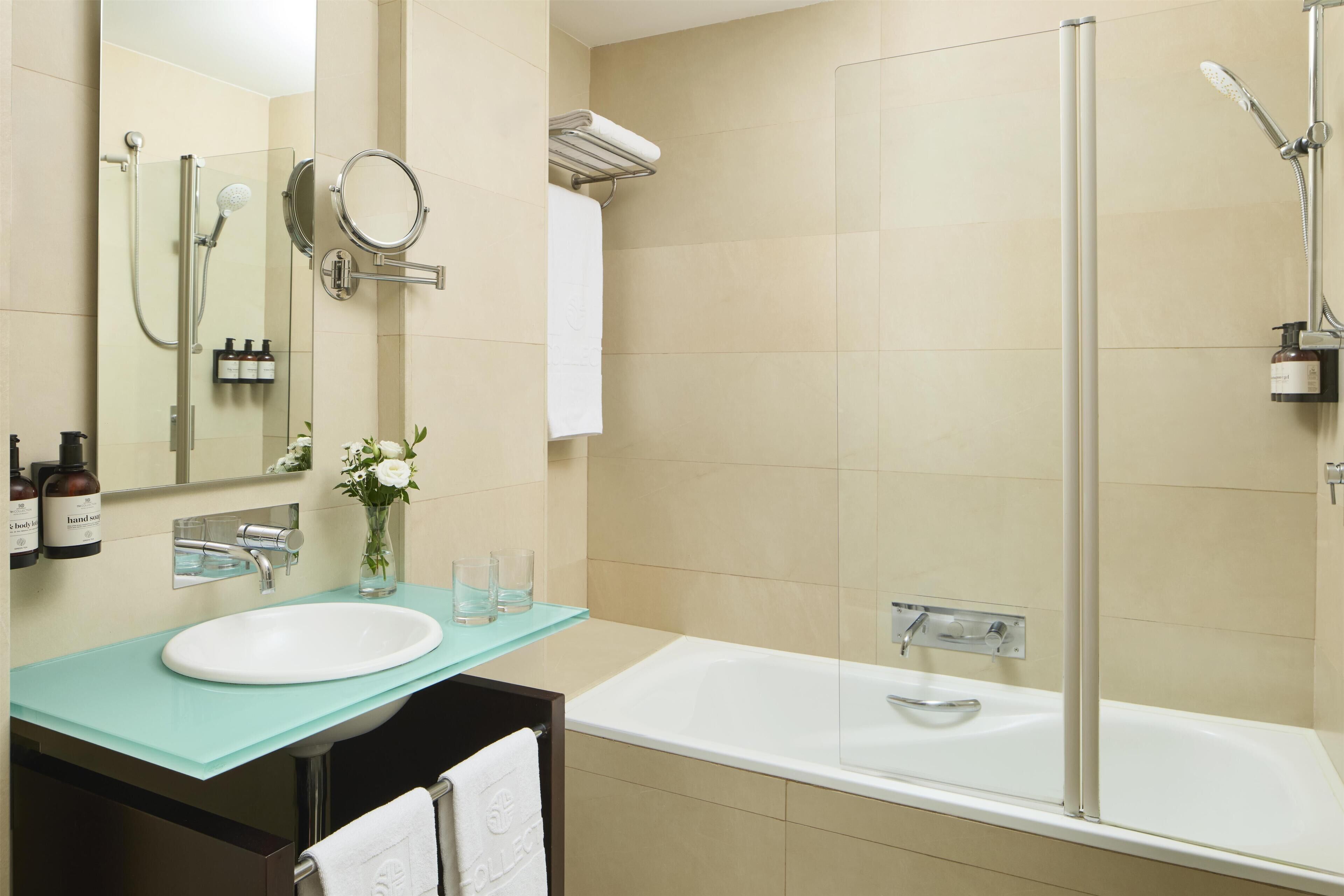 A modern bathroom with a glass countertop sink, a large mirror, a white bathtub, and a glass-enclosed shower area.