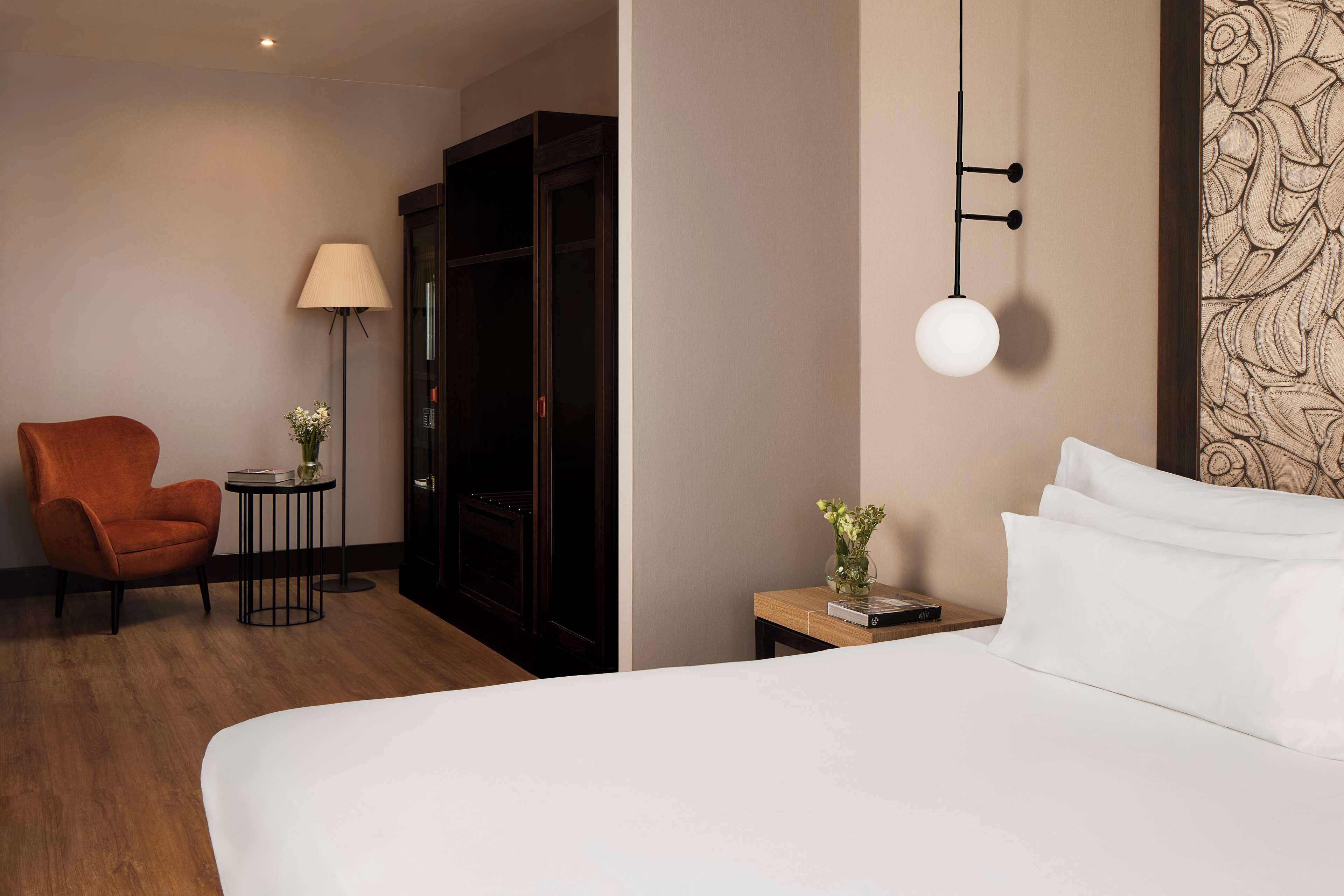 Habitación de hotel con una cama grande, una silla de madera, una mesita con lámpara y un armario.
