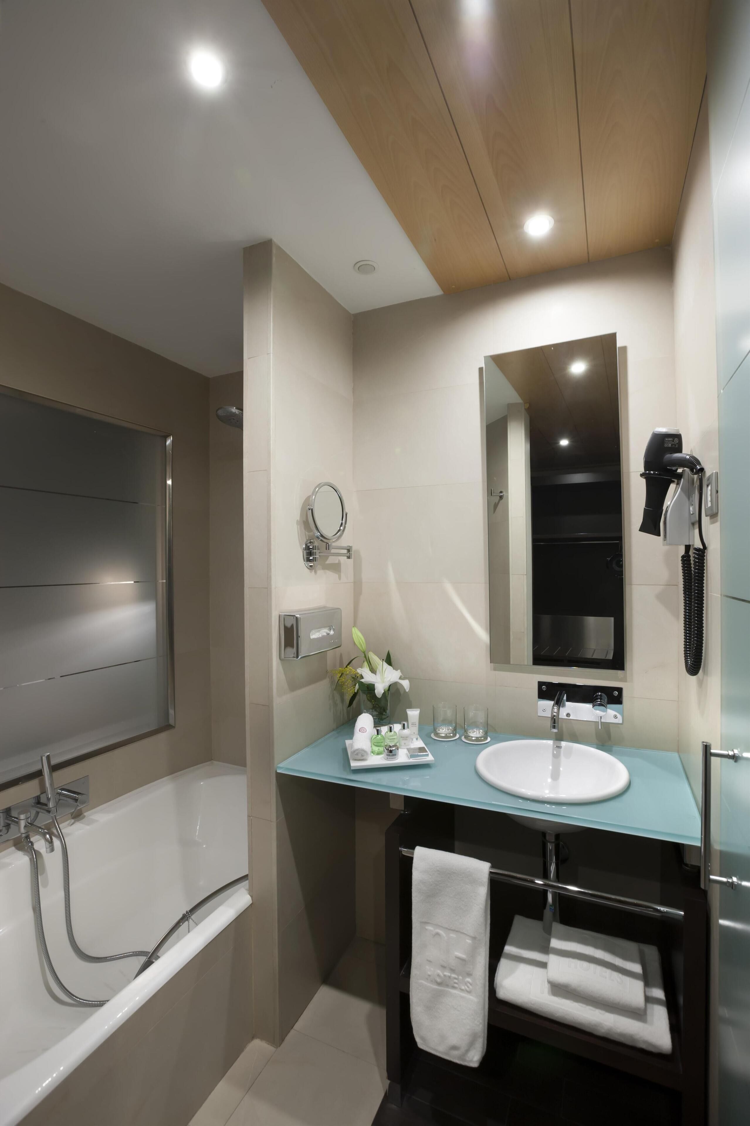 A modern bathroom with a glass vanity, a bathtub, a mirror, and a hairdryer.