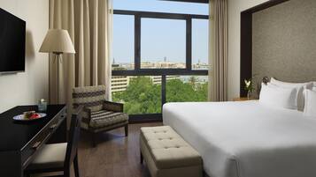 A hotel room with a bed, a desk, a chair, a TV, and a large window with a city view.