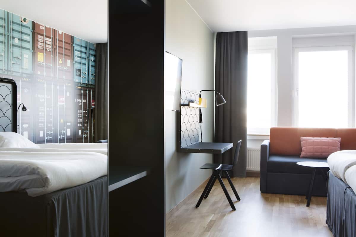 Una habitación de hotel con cama, escritorio, silla, sofá y un ventanal grande.