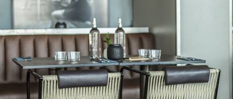 A dining area with a table set for two, two chairs with woven seats, a bottle, glasses, and a small plant.