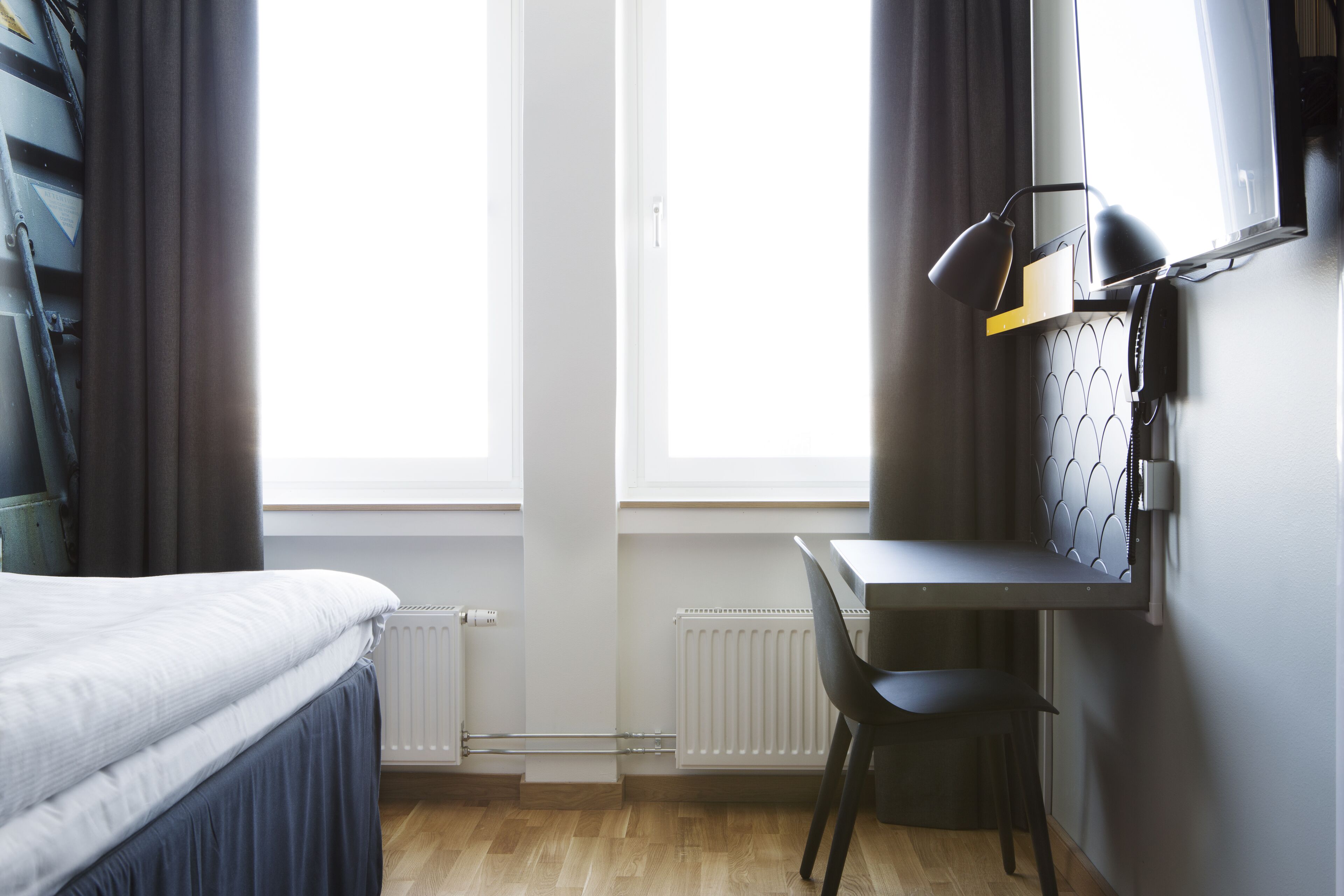 A bedroom with a bed, a desk, a chair, and a window with curtains.