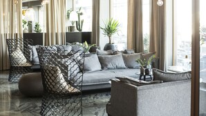 A modern living room with a grey sofa, a patterned chair, and a coffee table. There are plants and a view of the city through large windows. - Comfort Hotel Goteborg (Gothenburg)