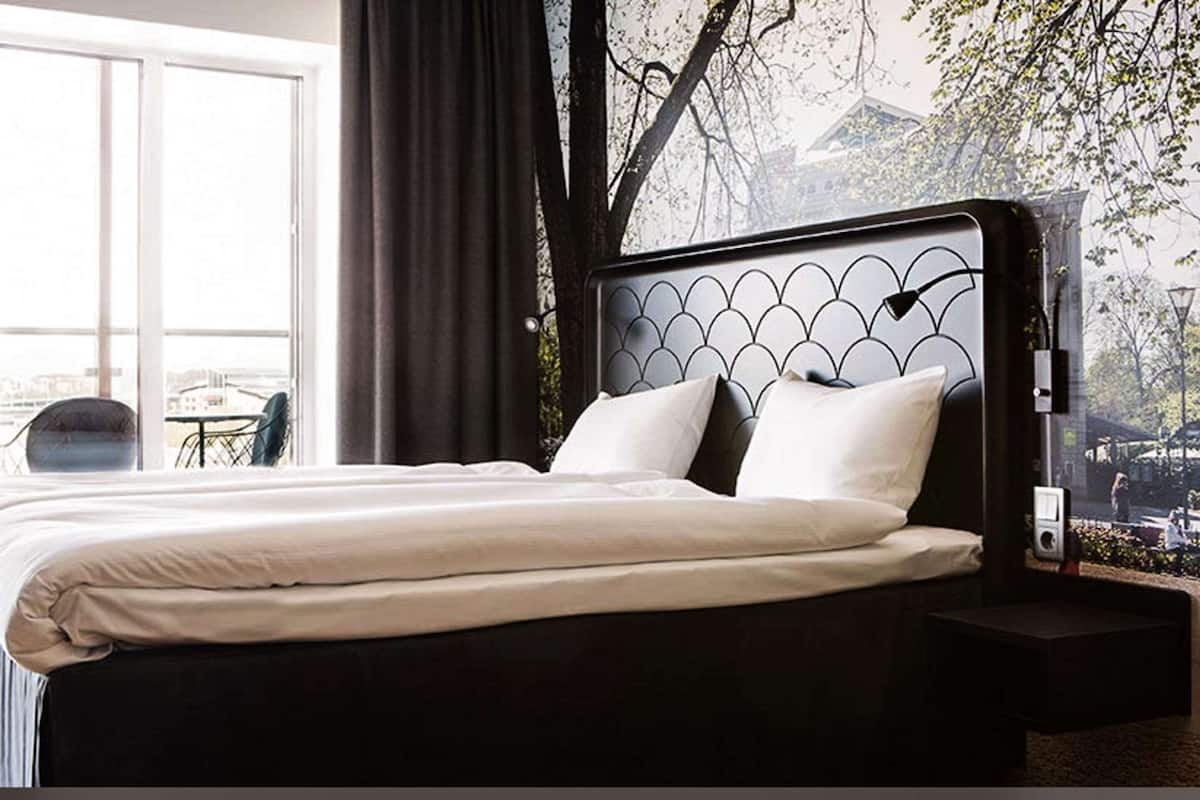Una habitación de hotel con una cama grande, vistas a la ciudad y una ventana con cortinas.