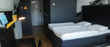 Una habitación de hotel con cama, escritorio y lámpara. Se ve una puerta que da a otra habitación.