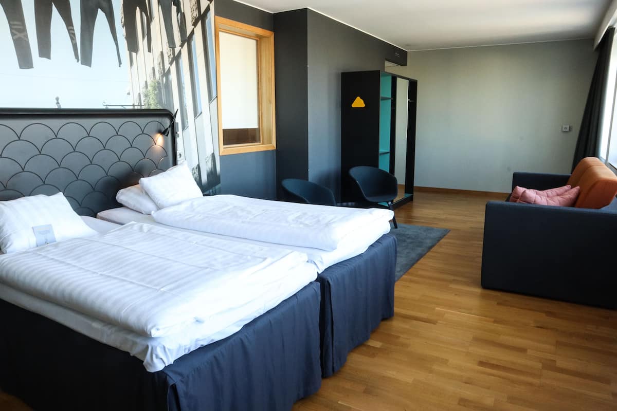 Una habitación de hotel moderna con dos camas, un sofá, un espejo y suelo de madera.