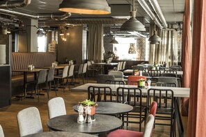 A modern restaurant interior with high tables, booths, and hanging pendant lights.