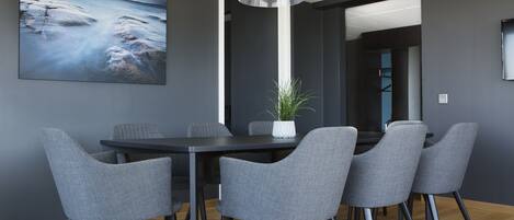 Un espace repas moderne avec une table de couleur gris foncé et des chaises assorties, un luminaire suspendu et un grand tableau abstrait accroché au mur.