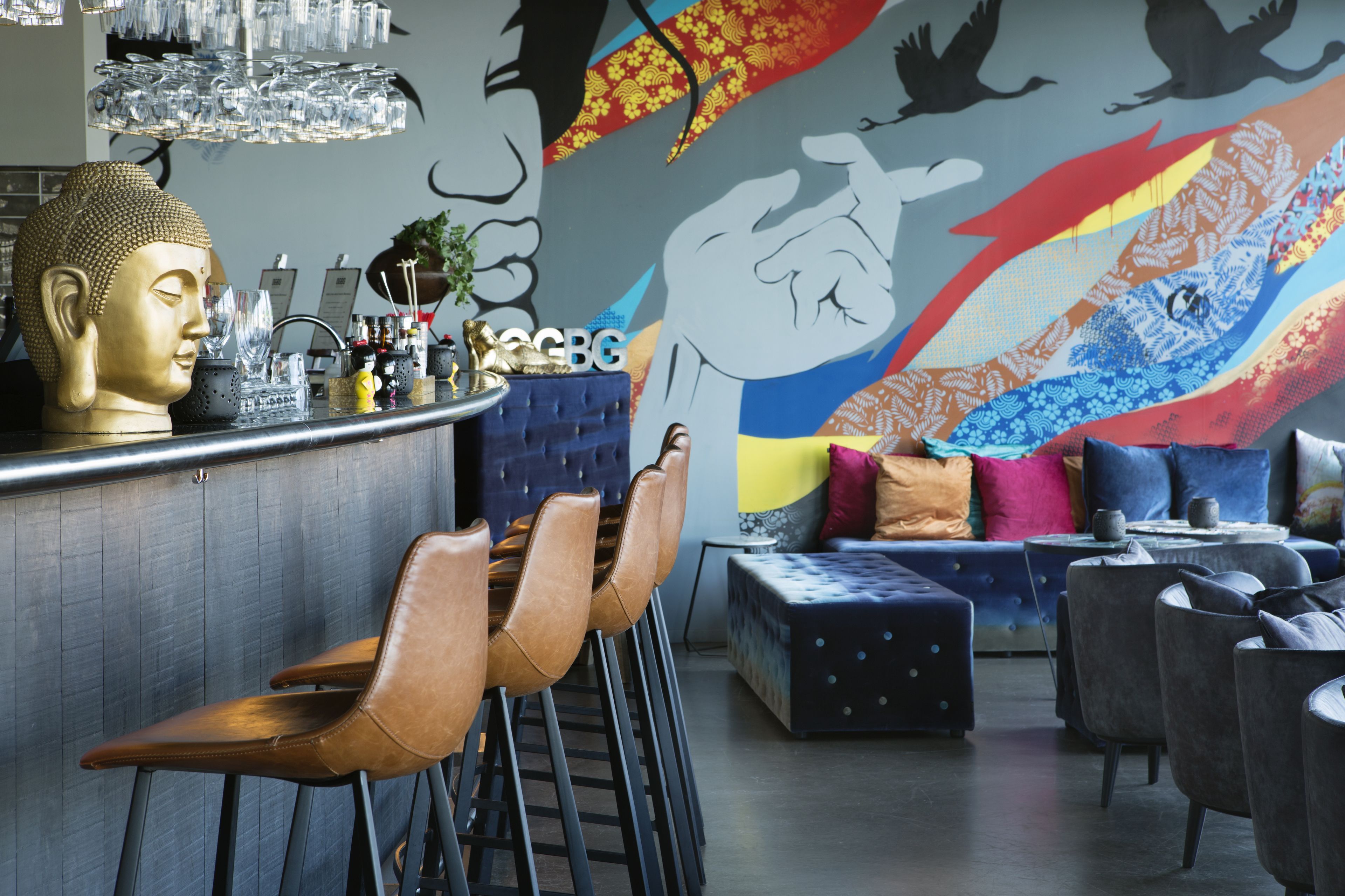 A bar area with a Buddha head sculpture, bar stools, and a colorful mural in the background.
