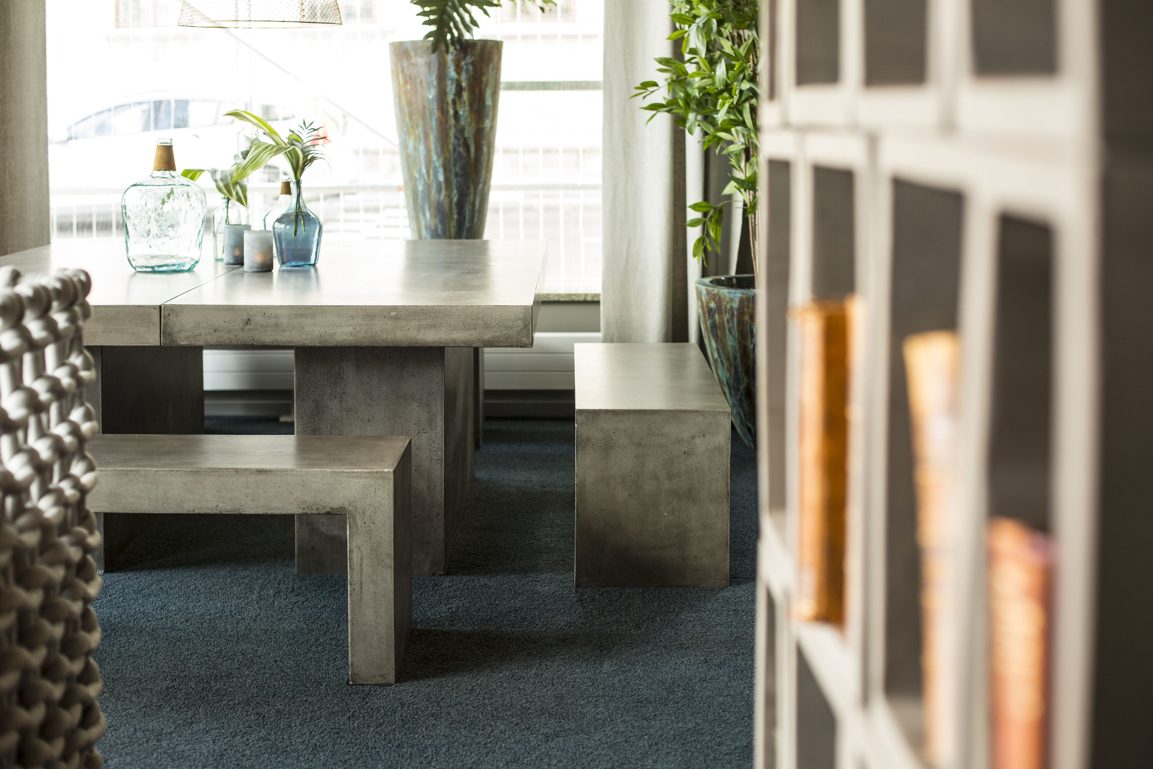 A modern interior with a concrete table, benches, and potted plants.