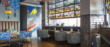 A bar area with seating, a wall with hanging ornaments, and shelves with bottles.
