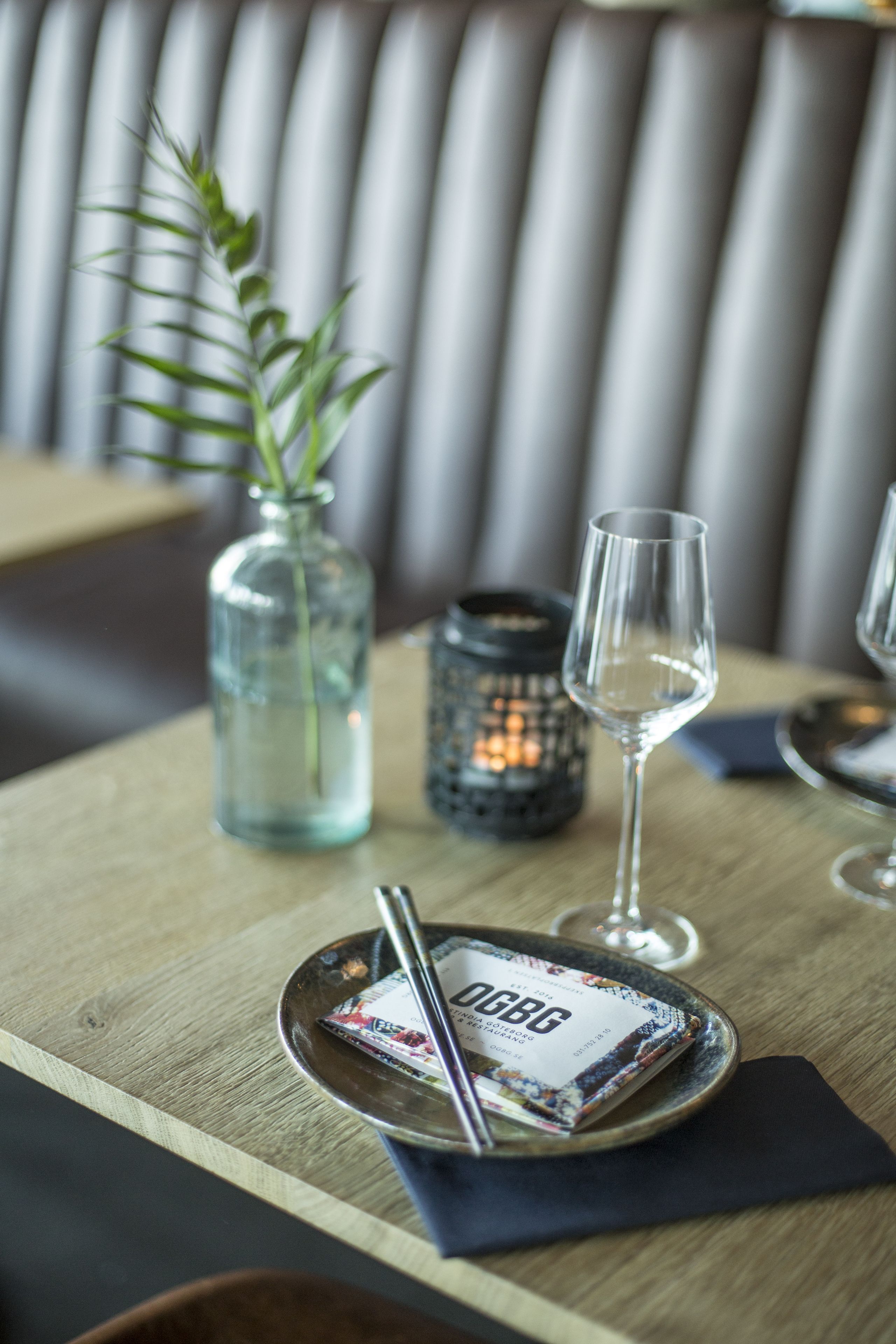 A dining table with a glass vase, a candle, and a wine glass.