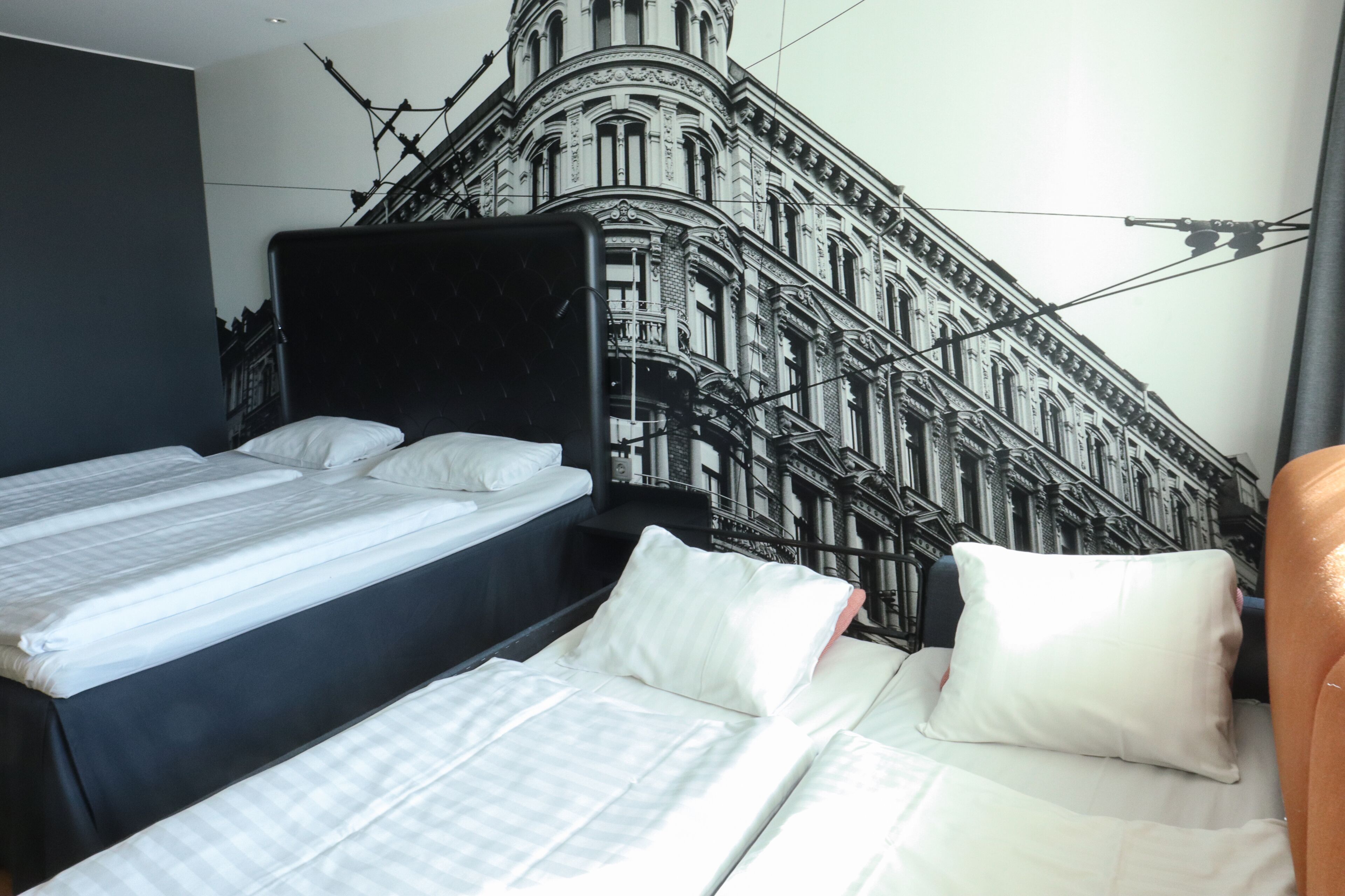 A hotel room with a bed, a chair, and a wall mural of a building.