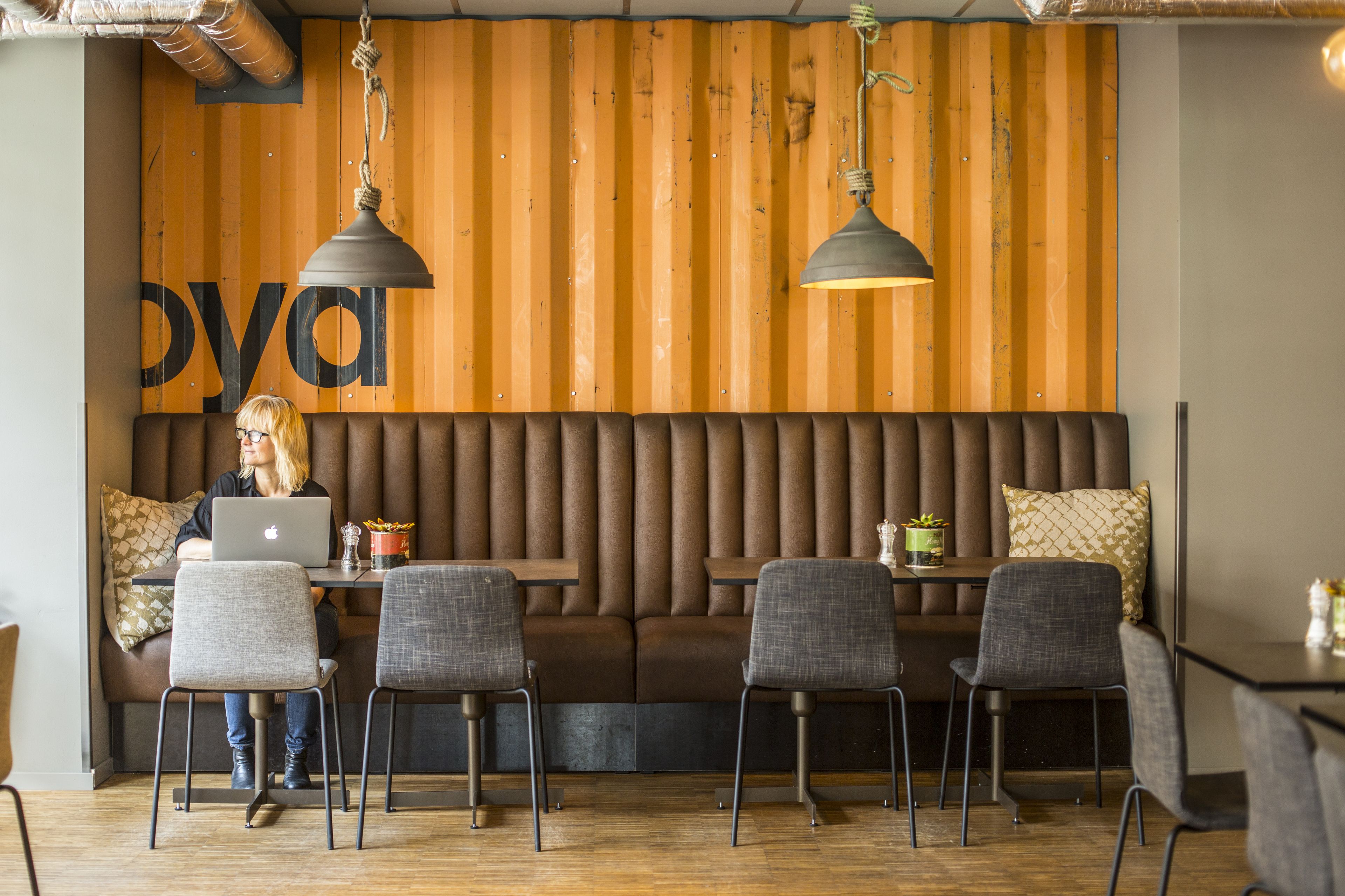 A modern seating area with a wooden wall, a laptop on a table, and a person working.