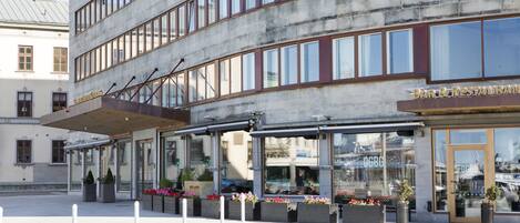 A multi-story building with a bar and restaurant on the ground floor, featuring large windows and outdoor seating with potted plants.