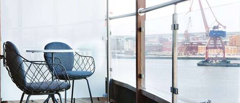 A balcony with a view of a port and cranes, featuring two chairs and a table.