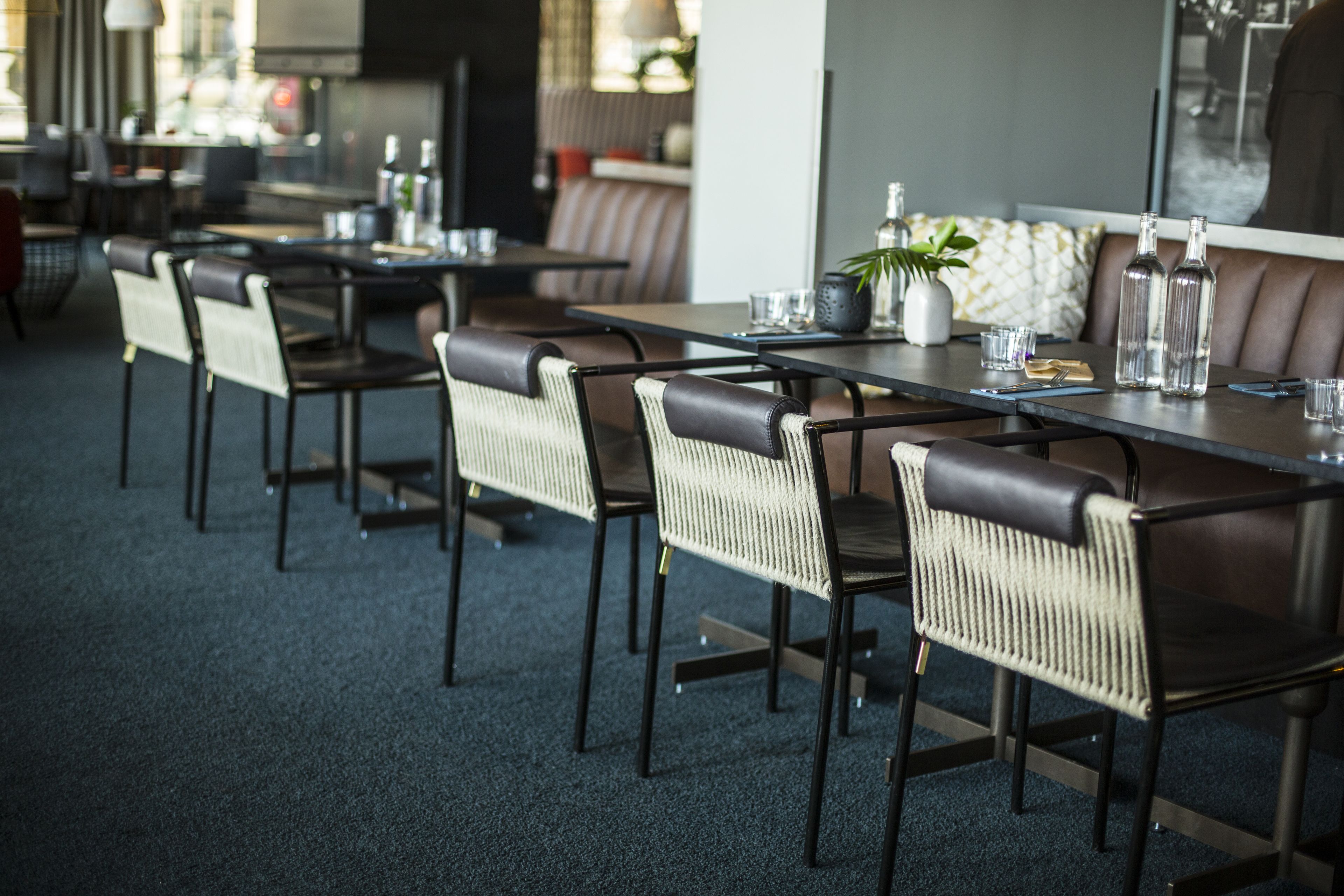 Un restaurante moderno con sillas y mesas de cuero oscuro, una planta en maceta y botellas sobre la mesa.