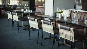 Un restaurant moderne avec des chaises et des tables en cuir foncé, une plante en pot et des bouteilles posées sur la table.