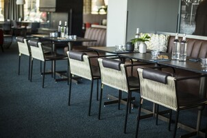 Un restaurante moderno con sillas y mesas de cuero oscuro, una planta en maceta y botellas sobre la mesa.