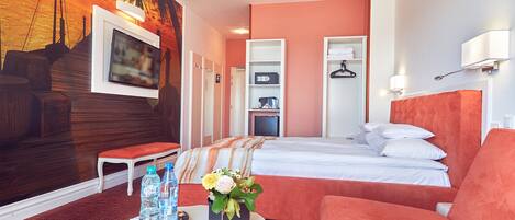 Habitación de hotel con cama, sofá, televisión, estante montado en la pared y un mural de atardecer en la pared.