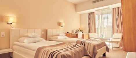 Una habitación de hotel con dos camas, un escritorio, una silla y un ventanal con cortinas.